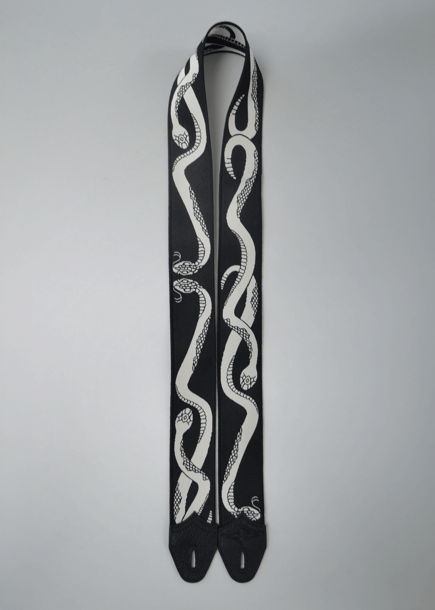 Black side of reversible snake jacquard guitar strap with black leather endcaps by Mary and Shelley