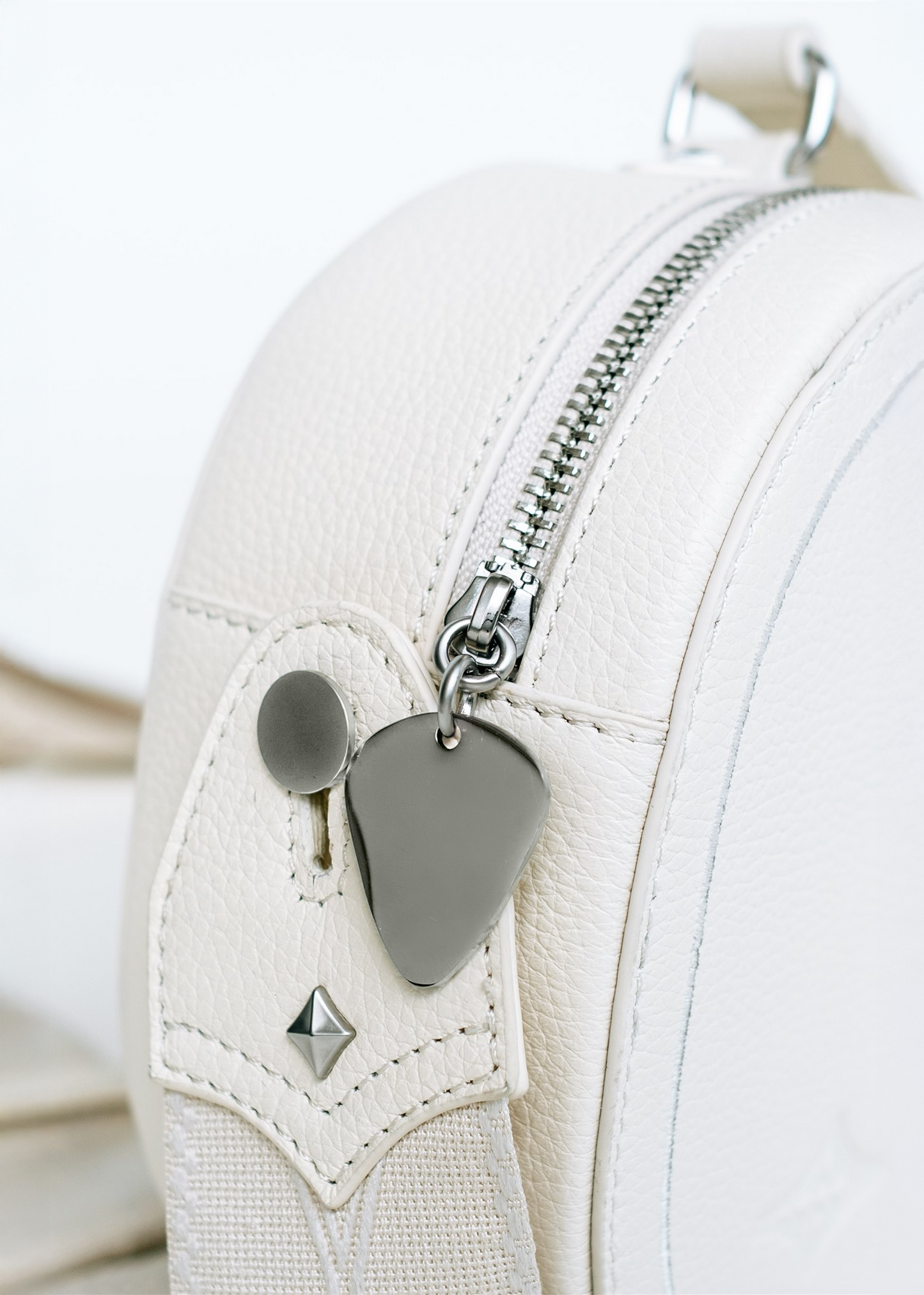 Close-up of Ivory Mary and Shelley Ritual Crossbody Bag showing real guitar strap attachment with patent-pending Strapbolt™ hardware, metal guitar pick zipper pull, and signature starburst stud.