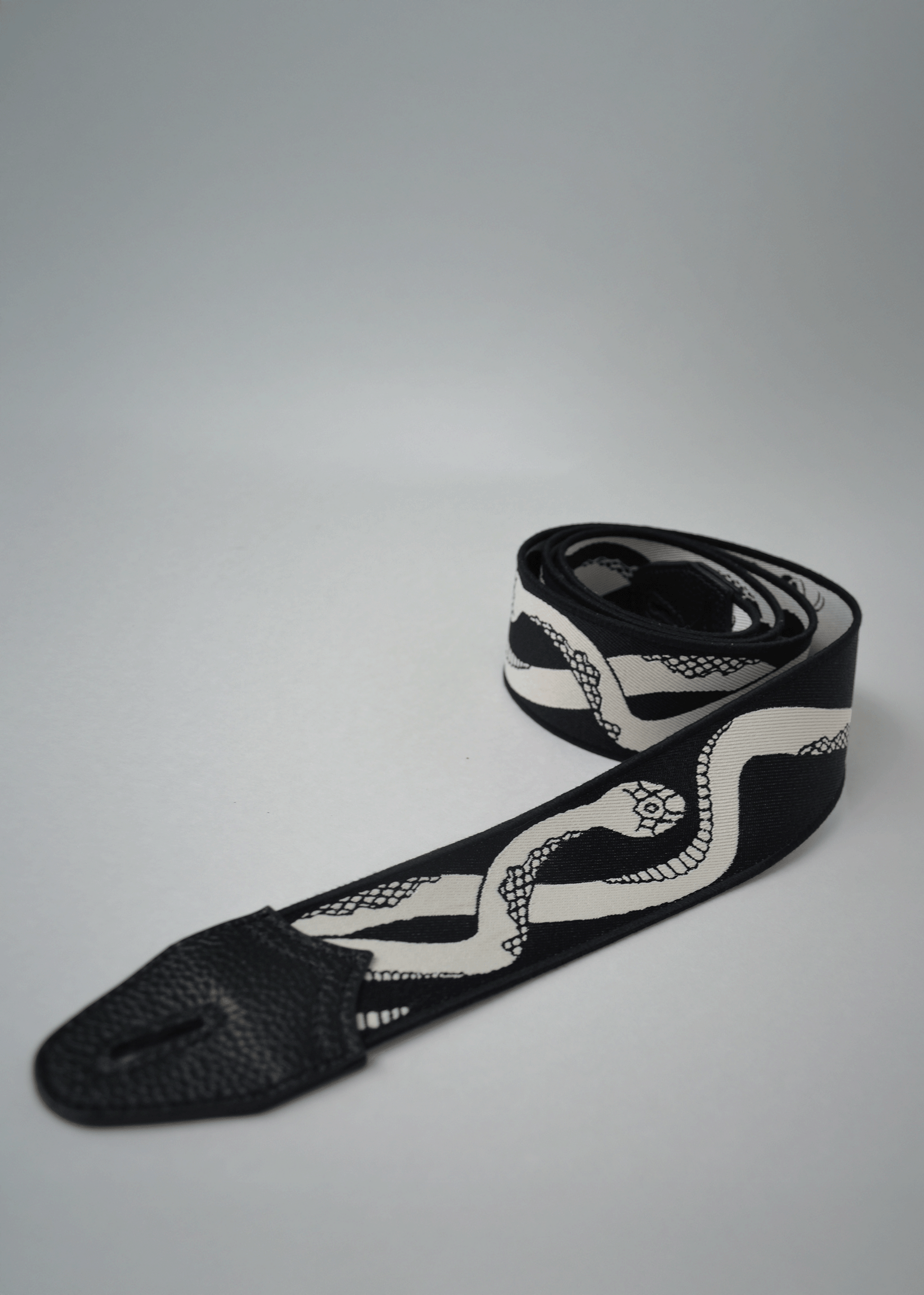 Rolled black side view of reversible snake jacquard guitar strap with black leather endcap by Mary and Shelley.