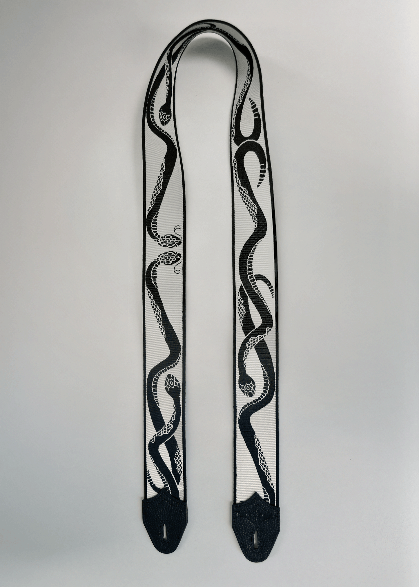 Ivory (white) side of reversible snake jacquard guitar strap with black leather endcaps by Mary and Shelley.