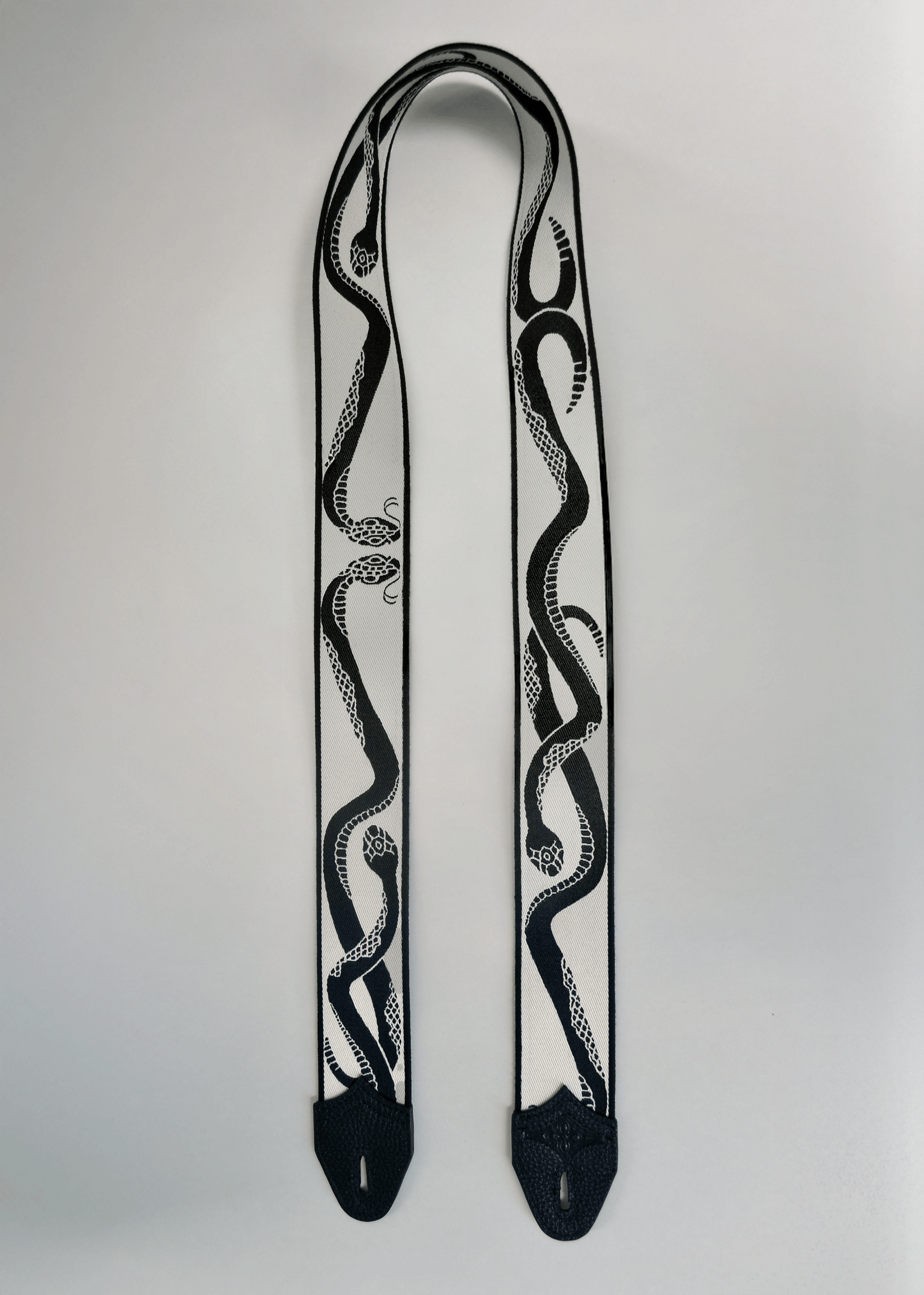 Ivory (white) side of reversible snake jacquard guitar strap with black leather endcaps by Mary and Shelley.