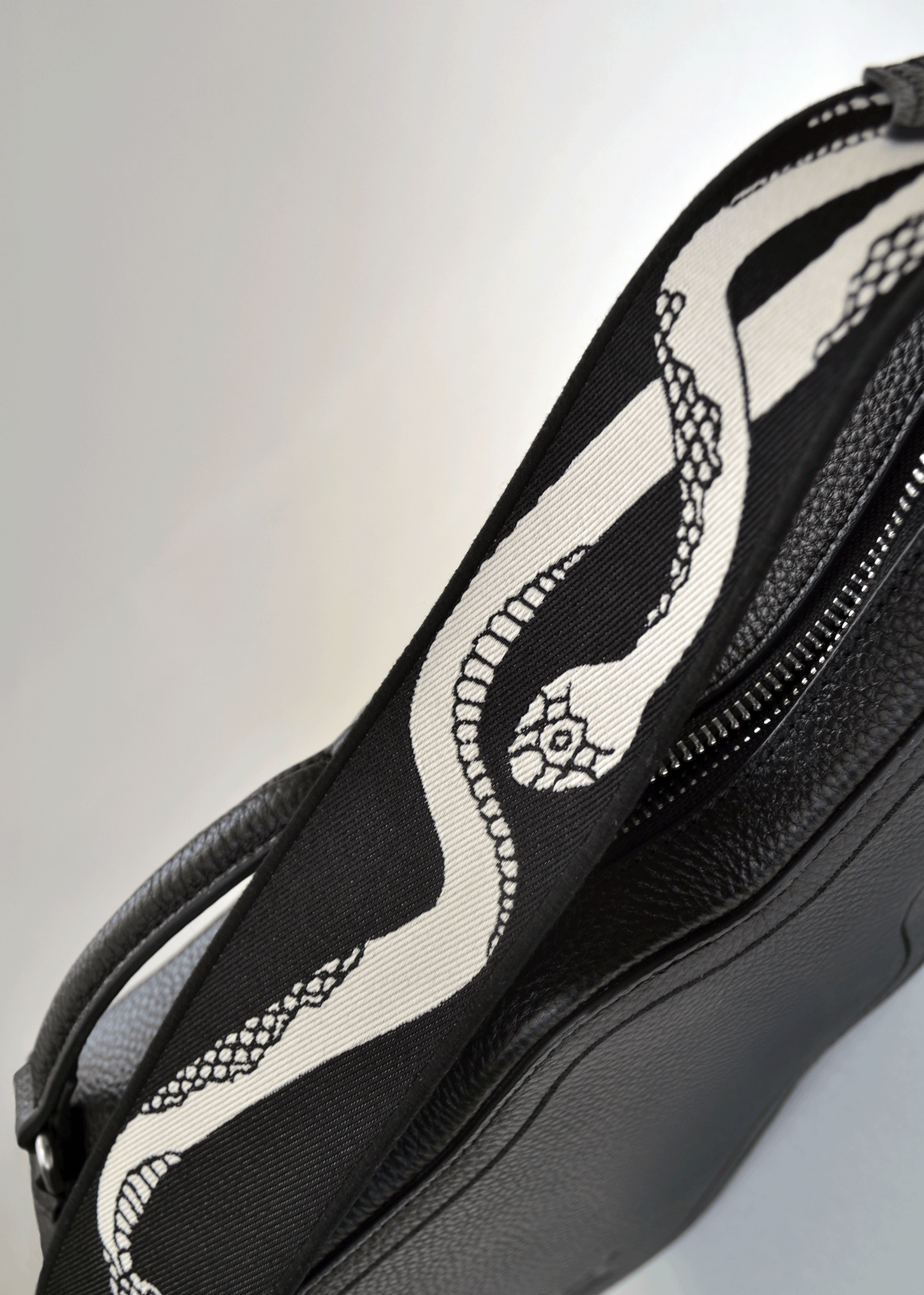 Ivory side of reversible snake jacquard guitar strap attached to black Mary and Shelley Ritual Bag.