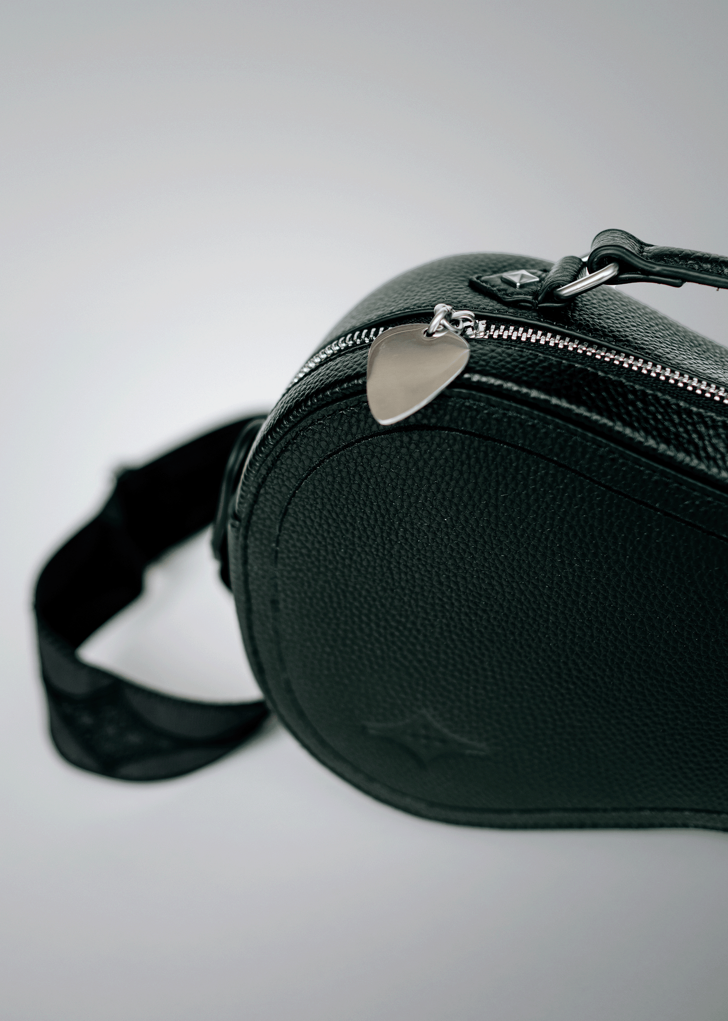 Close-up of black Mary and Shelley Ritual Crossbody Bag with silver metal guitar pick zipper pull, embossed logo, and jacquard strap detail.