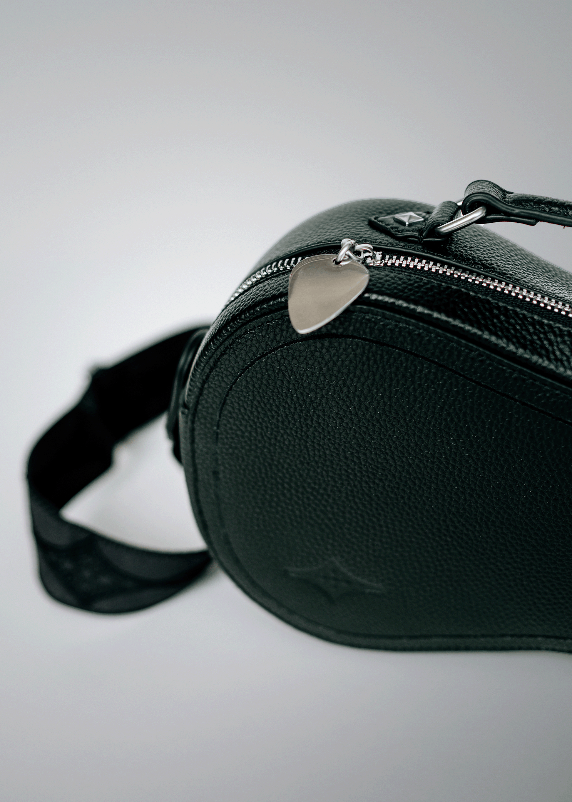 Close-up of black Mary and Shelley Ritual Crossbody Bag with silver metal guitar pick zipper pull, embossed logo, and jacquard strap detail.