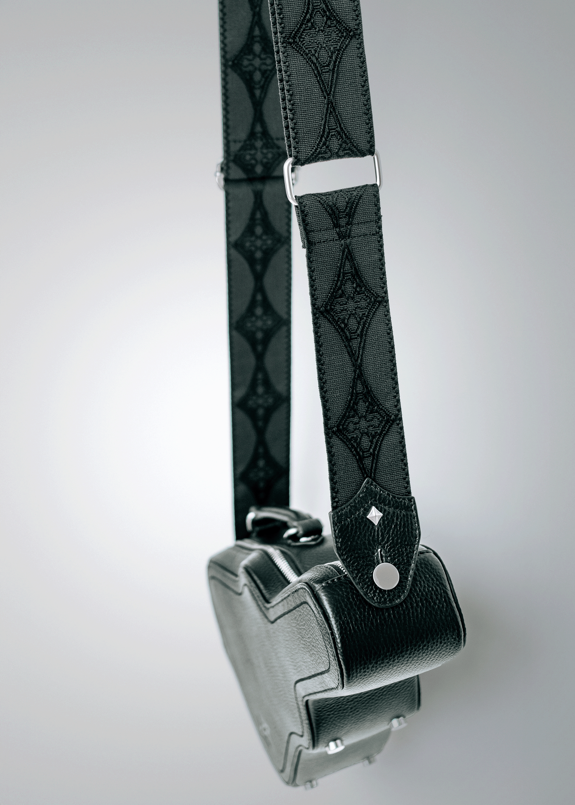 Close-up of black Mary and Shelley Ritual Crossbody Bag showing signature logo jacquard guitar strap with patent-pending Strapbolt™ hardware and starburst stud.