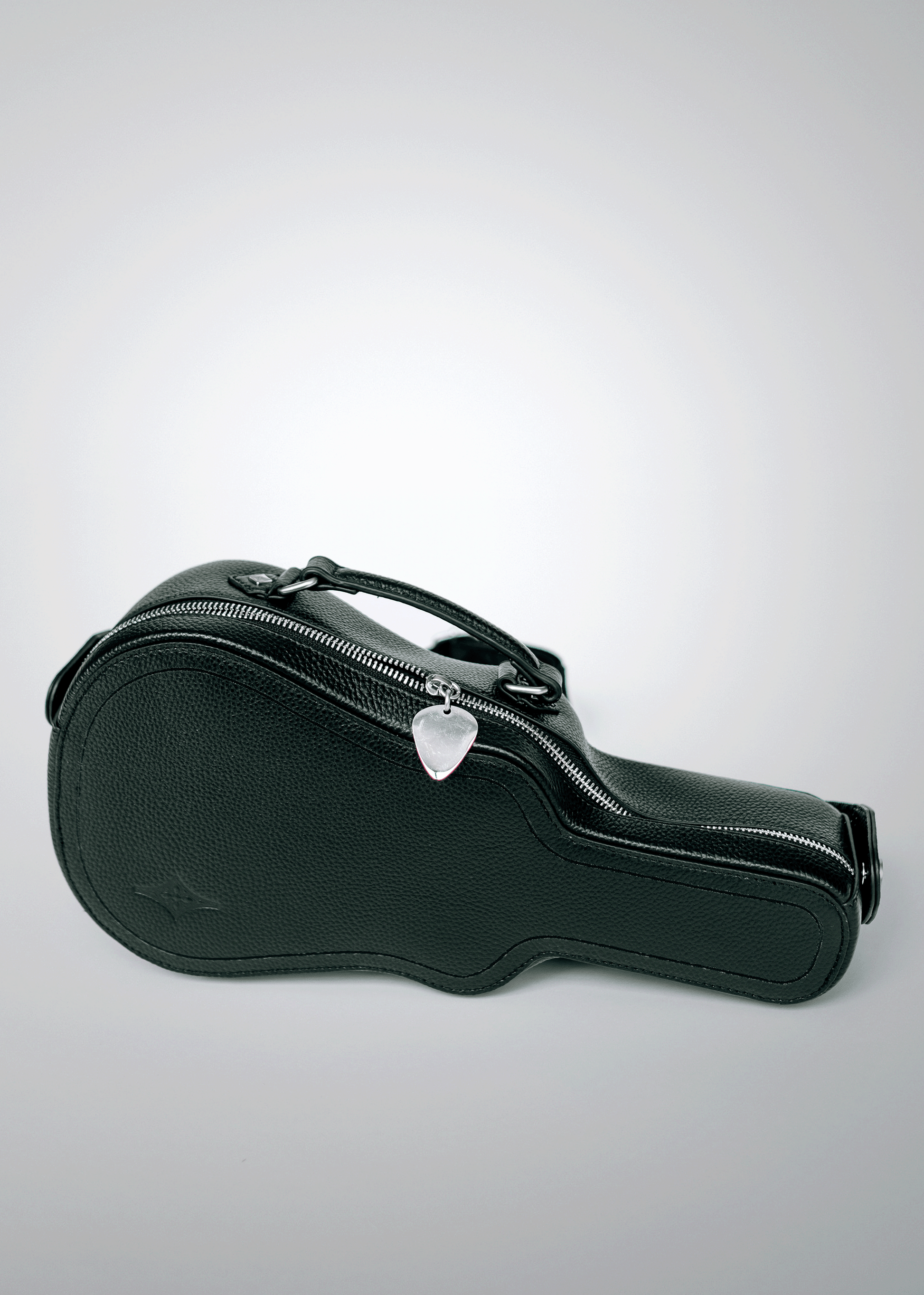 Black Mary and Shelley Ritual Crossbody Bag with guitar case silhouette, embossed logo detail, and silver metal guitar pick zipper pull, shown resting on ground.