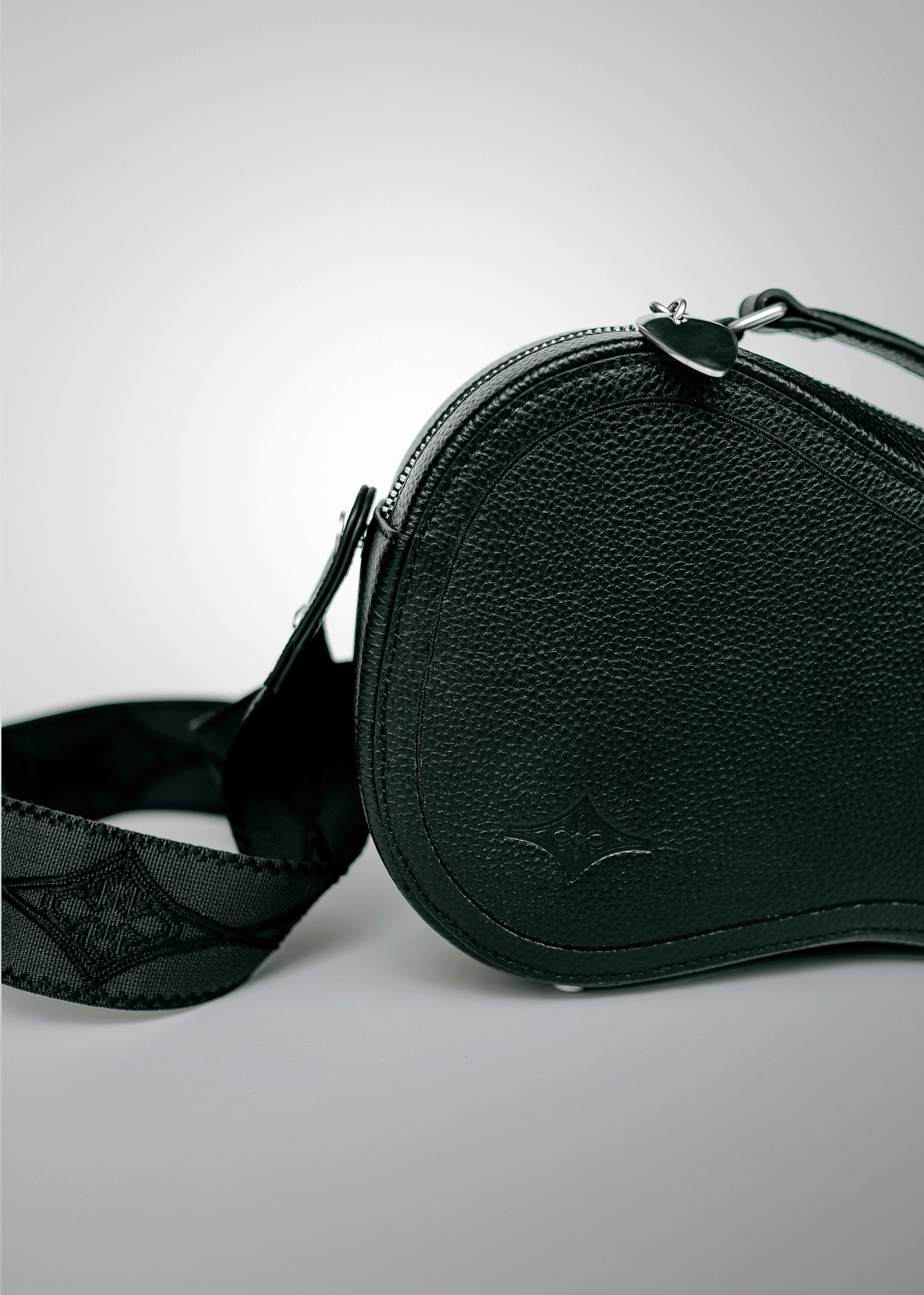 Close-up of black Mary and Shelley Ritual Crossbody Bag with embossed logo, silver metal guitar pick zipper pull, and jacquard logo guitar strap.