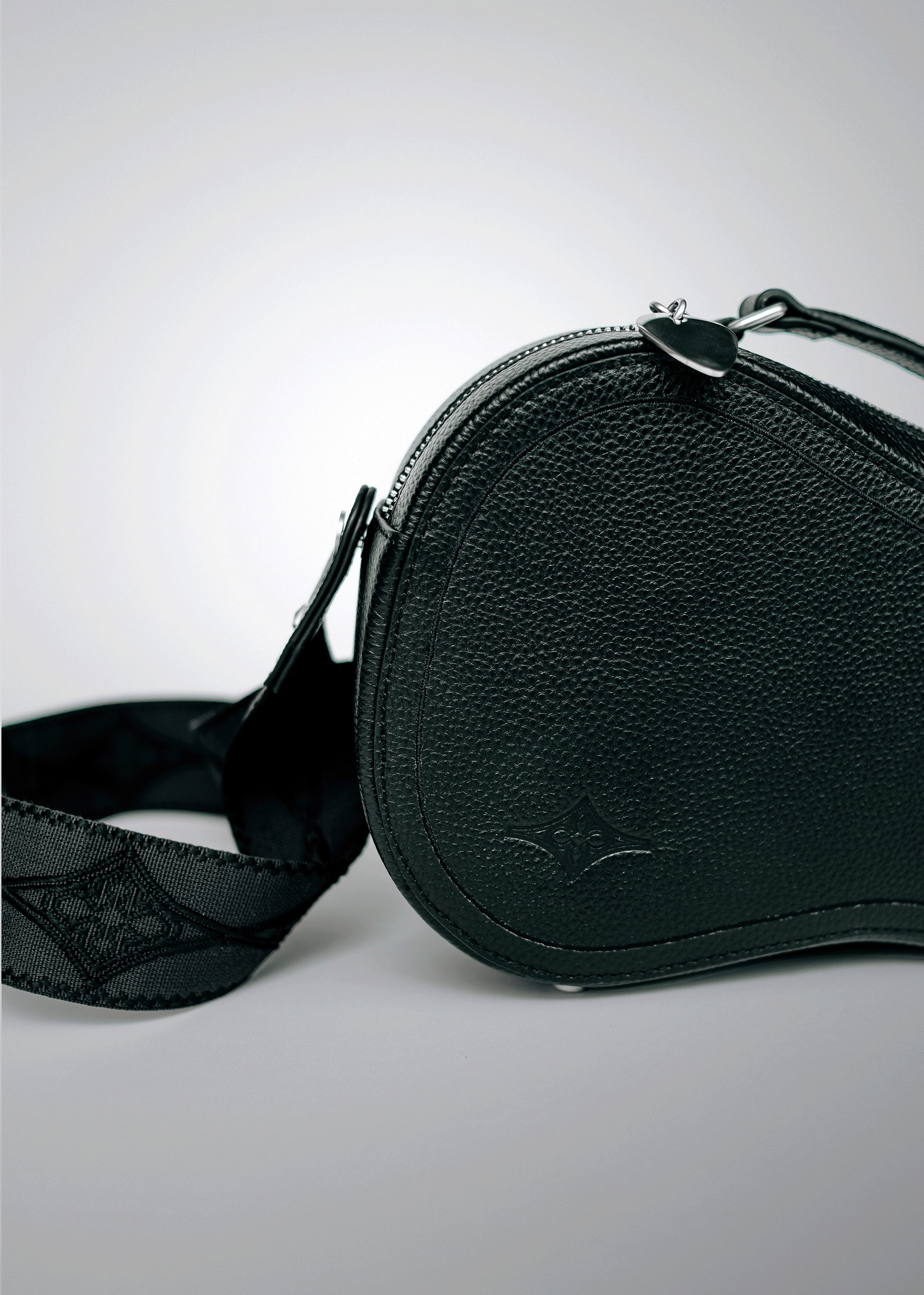 Close-up of black Mary and Shelley Ritual Crossbody Bag with embossed logo, silver metal guitar pick zipper pull, and jacquard logo guitar strap.