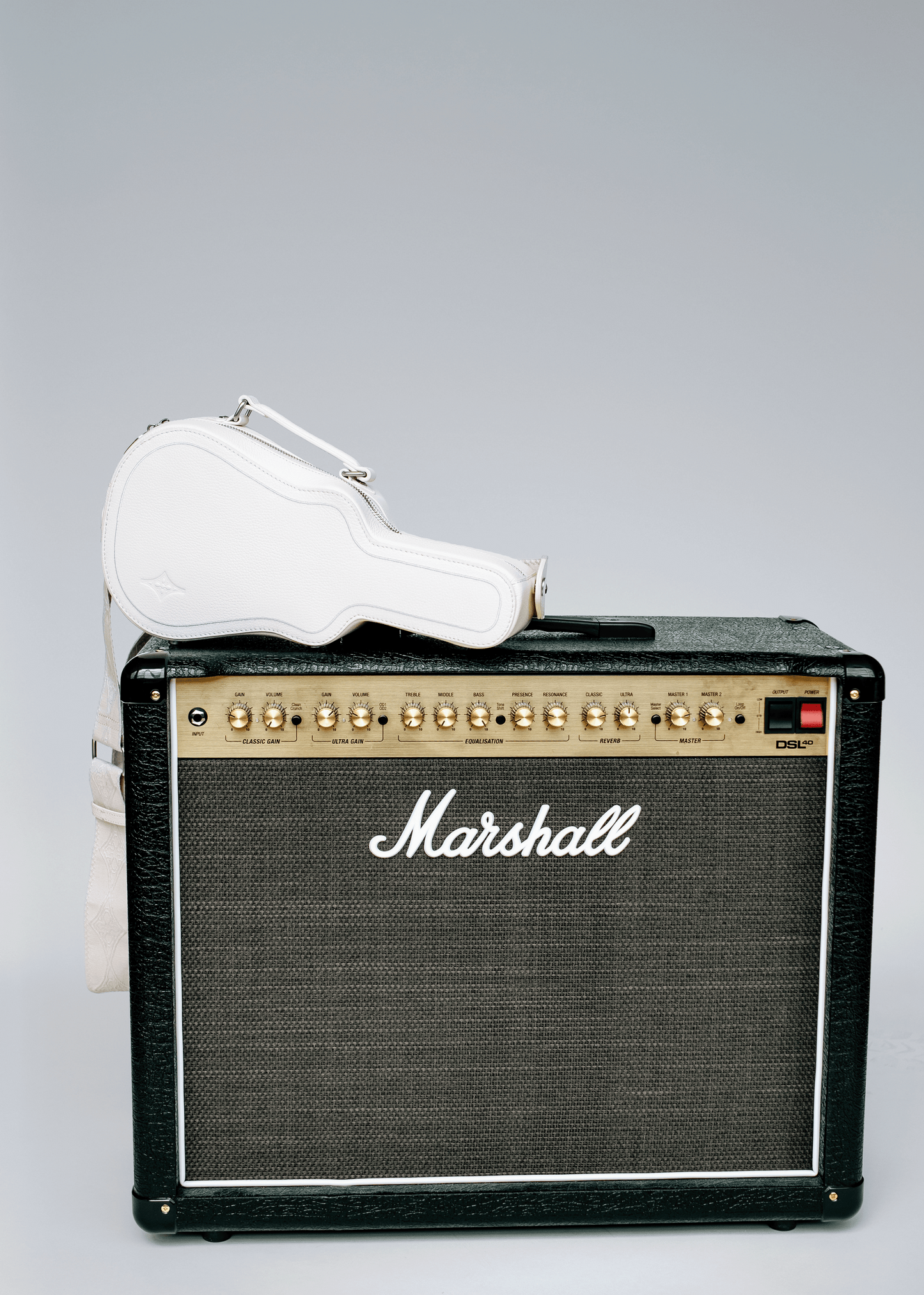 White Mary and Shelley Ritual Crossbody Bag with guitar case silhouette, styled resting on a black amplifier.