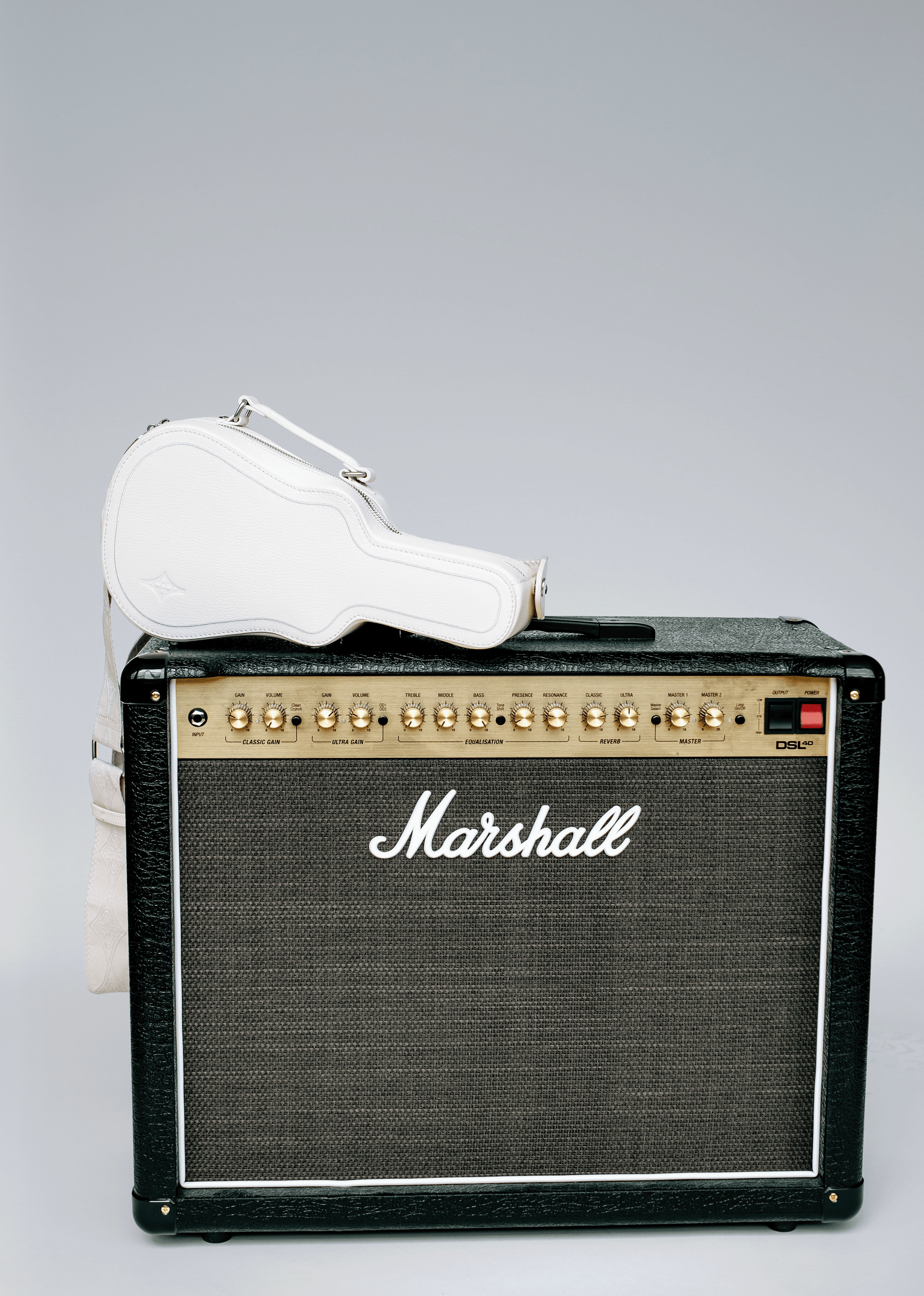 White Mary and Shelley Ritual Crossbody Bag with guitar case silhouette, styled resting on a black amplifier.